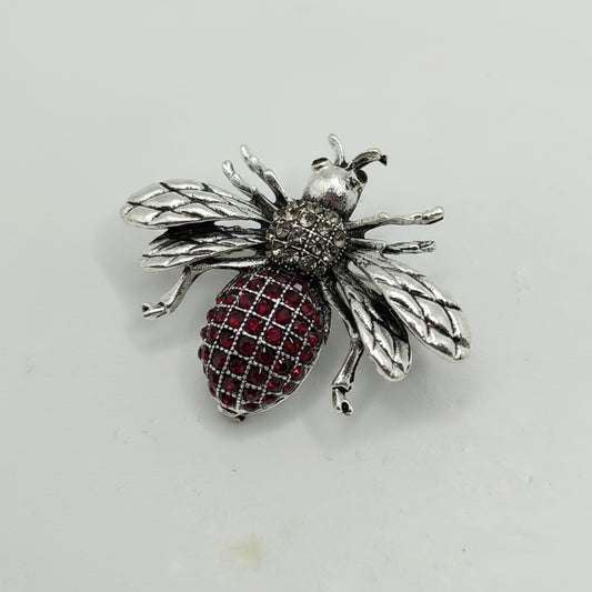 Silver bee-shaped brooch with red gemstones on a light gray background