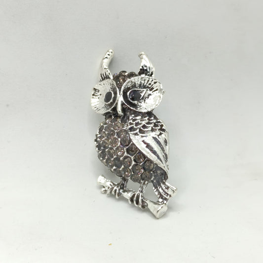 Silver owl-shaped brooch on a light gray background