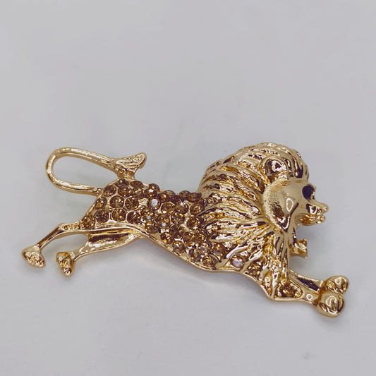 A gold tone brooch shaped like a lion, adorned with clear crystals.