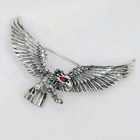 A silver-plated brooch in the shape of a flying eagle with a red eye detail.