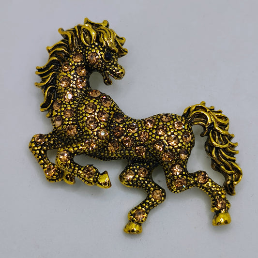 A brooch shaped like a galloping horse with diamante detailing on a bronze-colored background.