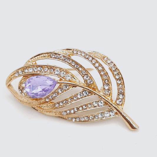 Gold leaf-shaped brooch with a purple gemstone on a light gray background