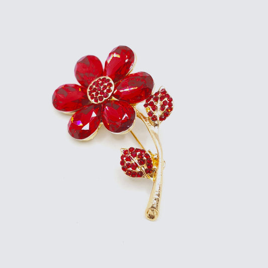 Red floral brooch with gold accents on a light gray background