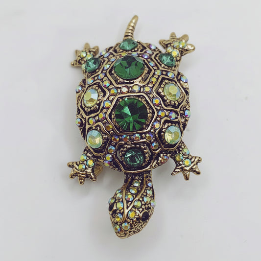 Decorative turtle-shaped pendant with green and gold gemstones on a white background