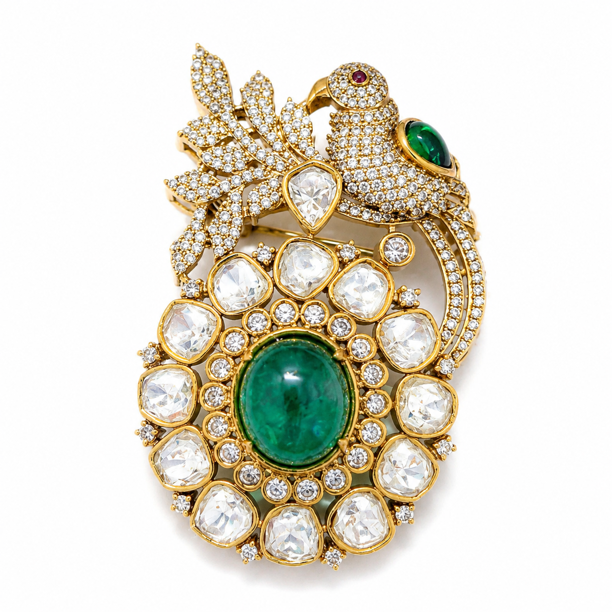 An ornate gold brooch featuring a bird perched on a leafy branch, set with numerous clear pavé diamonds and large emerald-cut green gemstones, photographed on a clean white background.