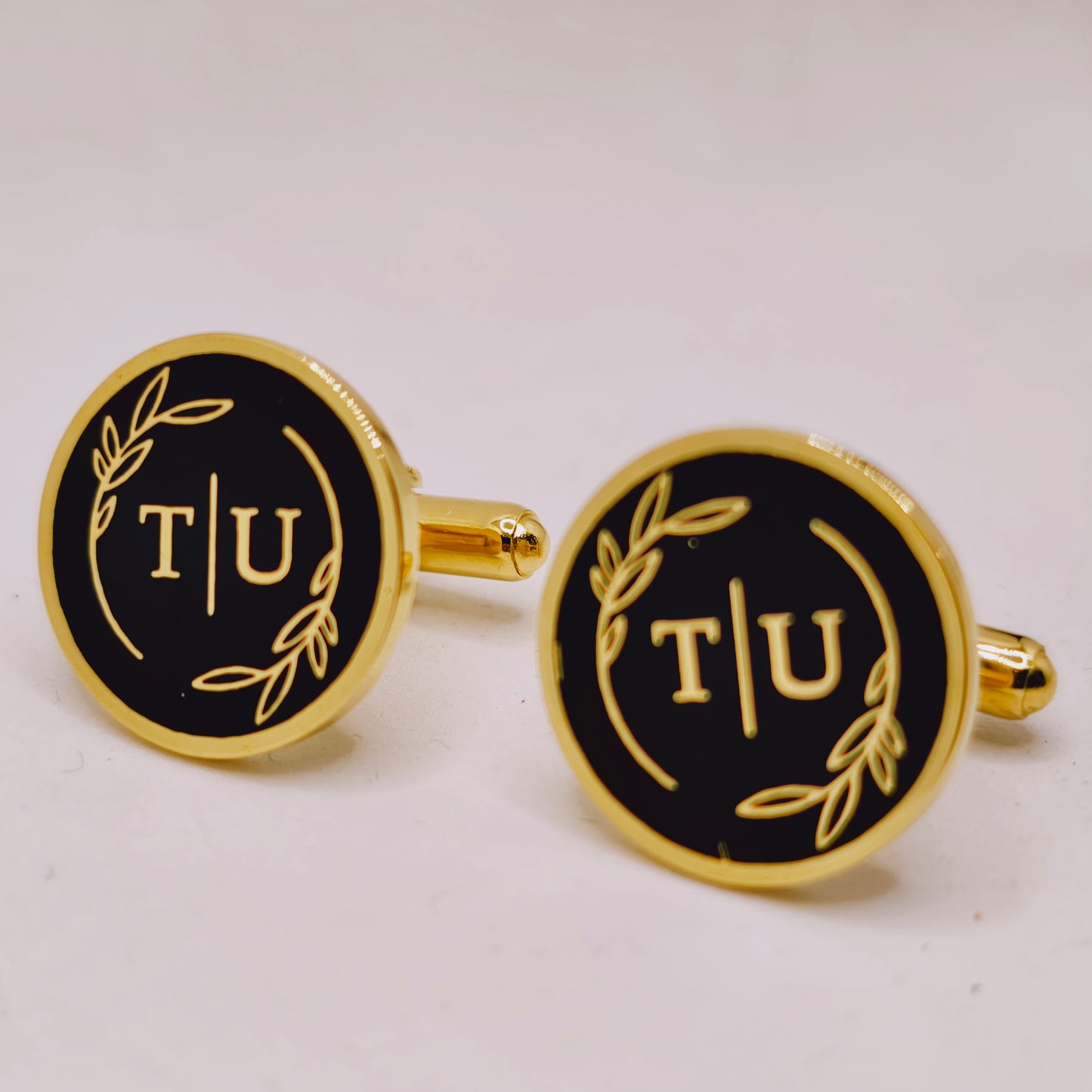 Gold and black cufflinks with 'T/U' initials on a white background