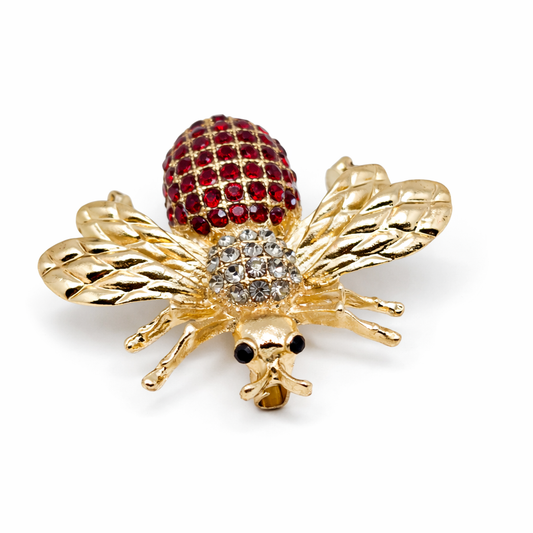 Gold bee-shaped brooch with red gemstones on a white background