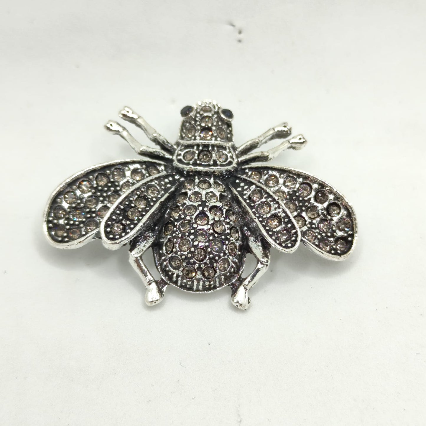 Silver insect-shaped brooch with gemstones on a white background