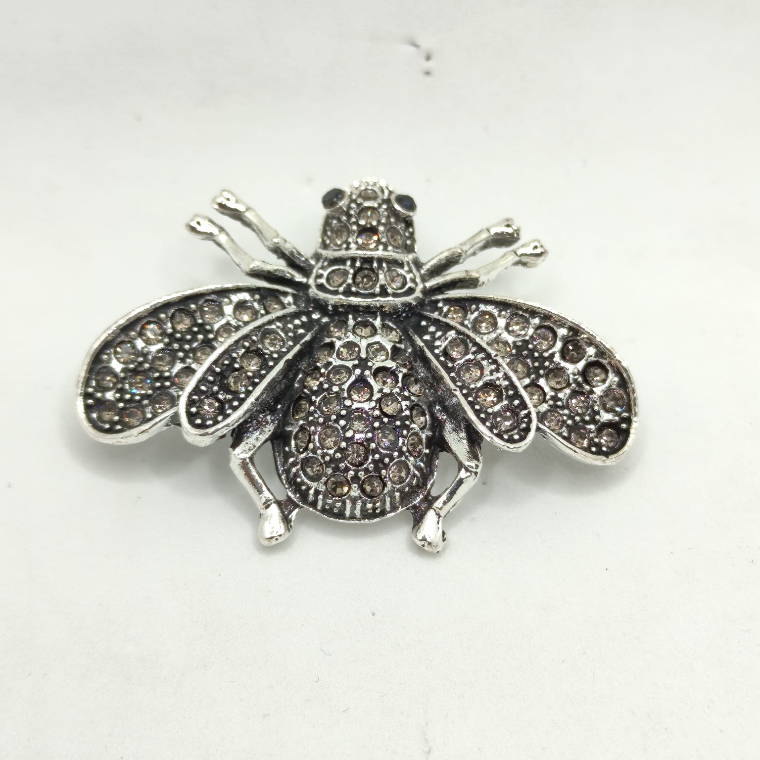 Silver insect-shaped brooch with gemstones on a white background