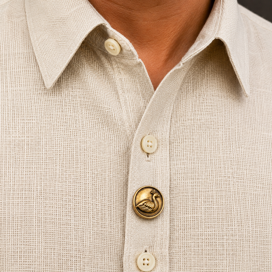 Close-up of a beige shirt with decorative buttons, including a gold one with a bird design.