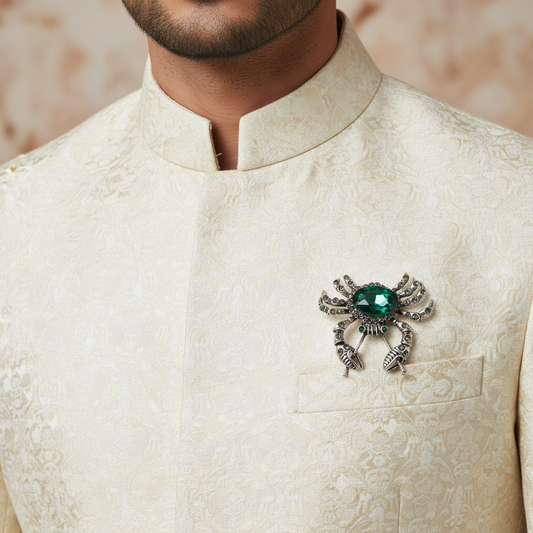 Silver spider-shaped brooch with a green gemstone on a light gray background