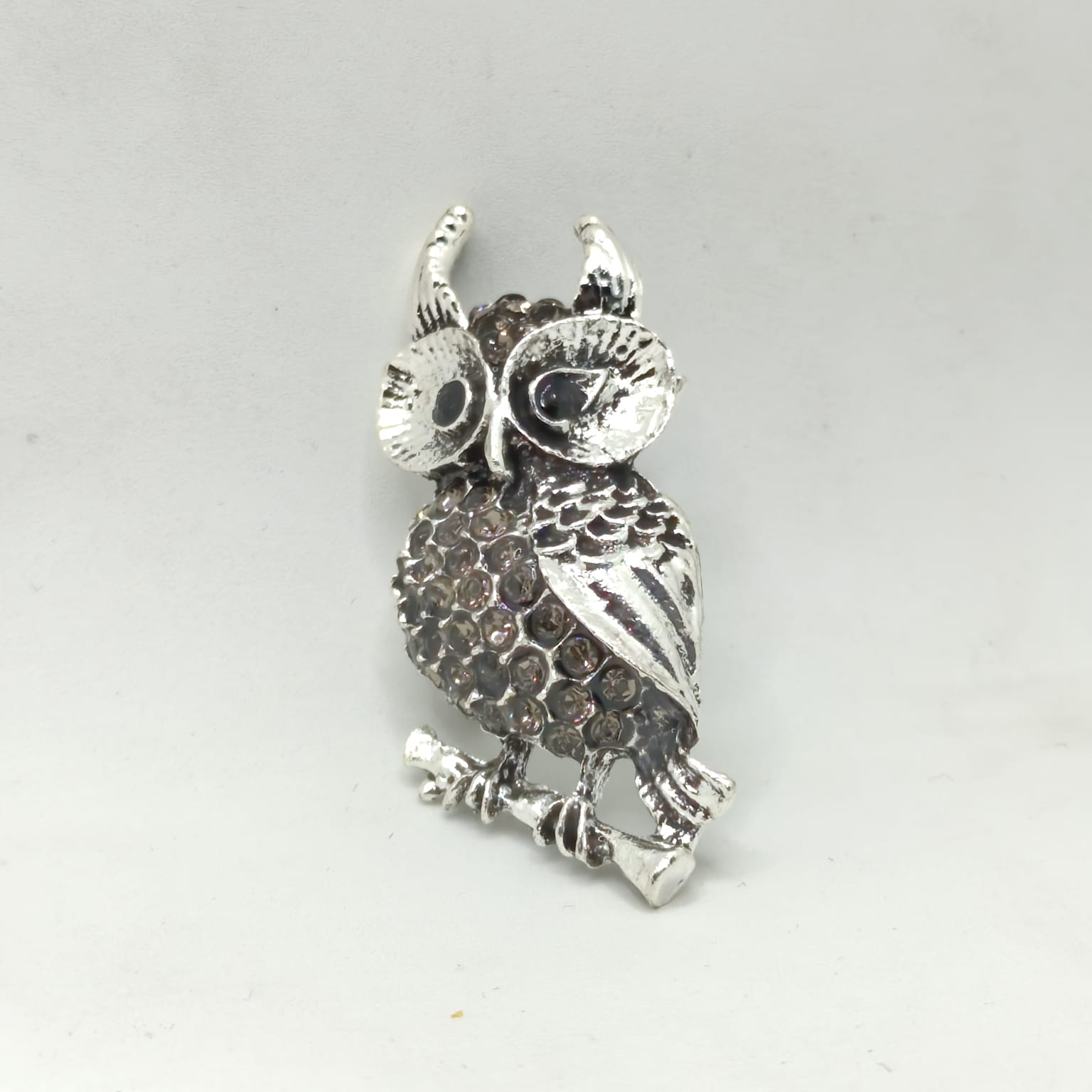 Silver owl-shaped brooch on a light gray background