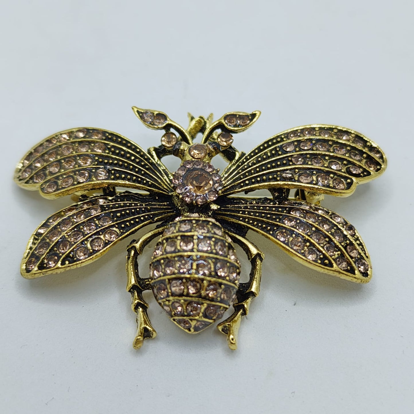 Gold bee-shaped brooch with brown rhinestones on a light gray background