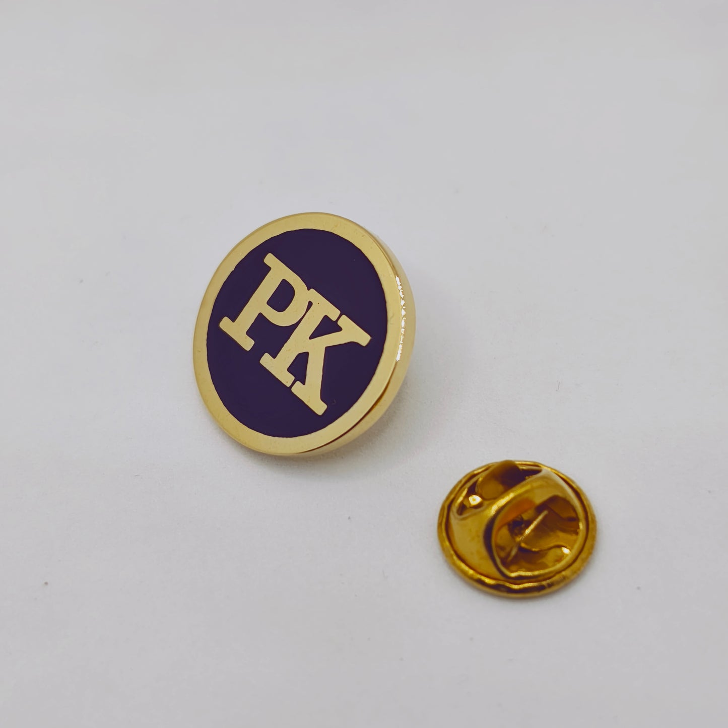 Gold and purple pin with 'PK' on a white background
