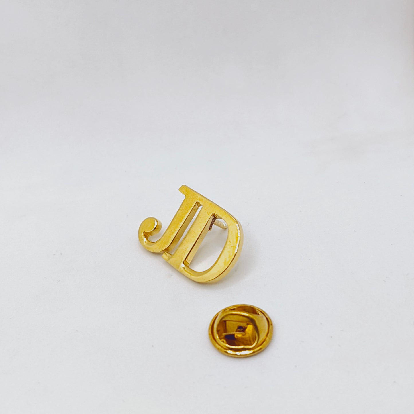 Gold letter 'J' pin on a white background
