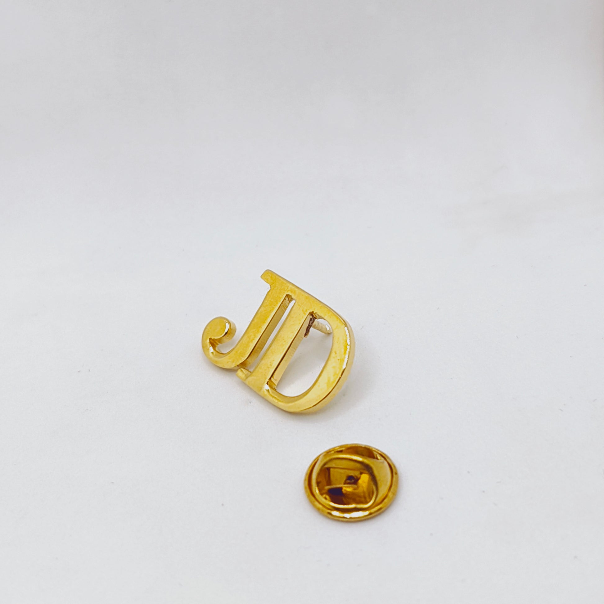 Gold letter 'J' pin on a white background